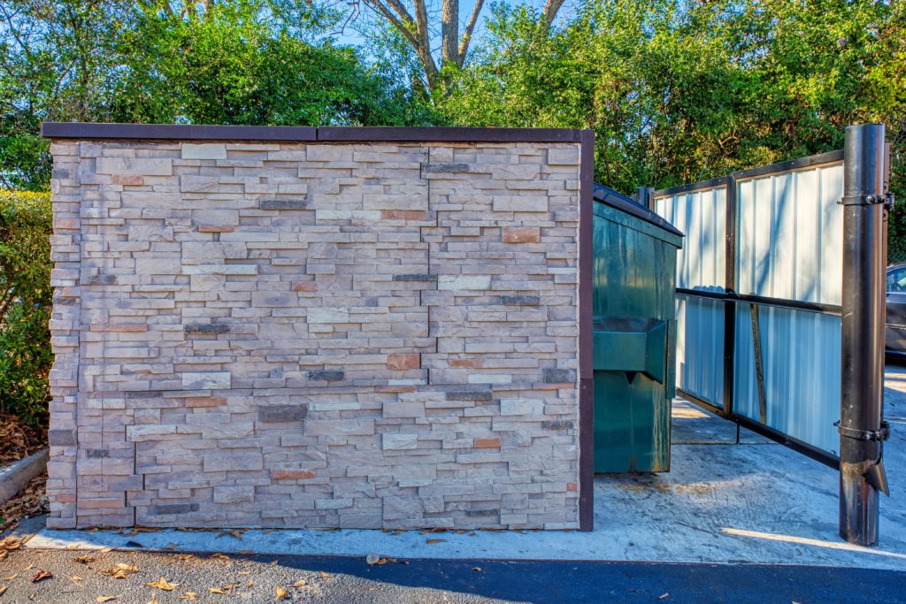 stacked stone dumpster enclosure with green dumpster and man door