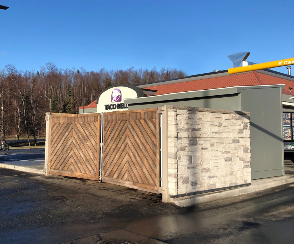 grey ledge stone dumpster enclosure with slanted wood gates in front of Taco Bell